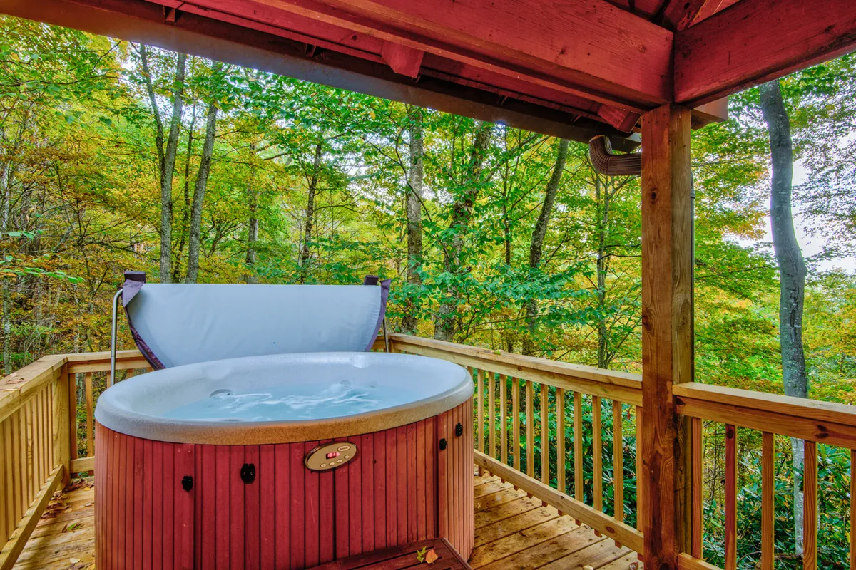 A hot tub nestled on a wooden deck, surrounded by towering trees, offering a secluded and serene retreat. The setting is designed for ultimate relaxation, inviting guests to stargaze or enjoy tranquil moments in bubbling warmth.