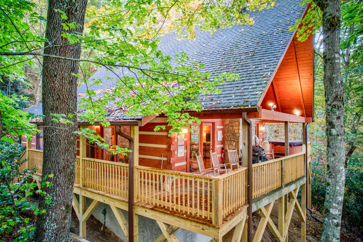 An inviting exterior shot that highlights the wooden deck and log cabin structure, set amid tall trees with a balcony railing suggesting openness and community. The space is ideal for relaxing, stargazing, and hosting friends or family.