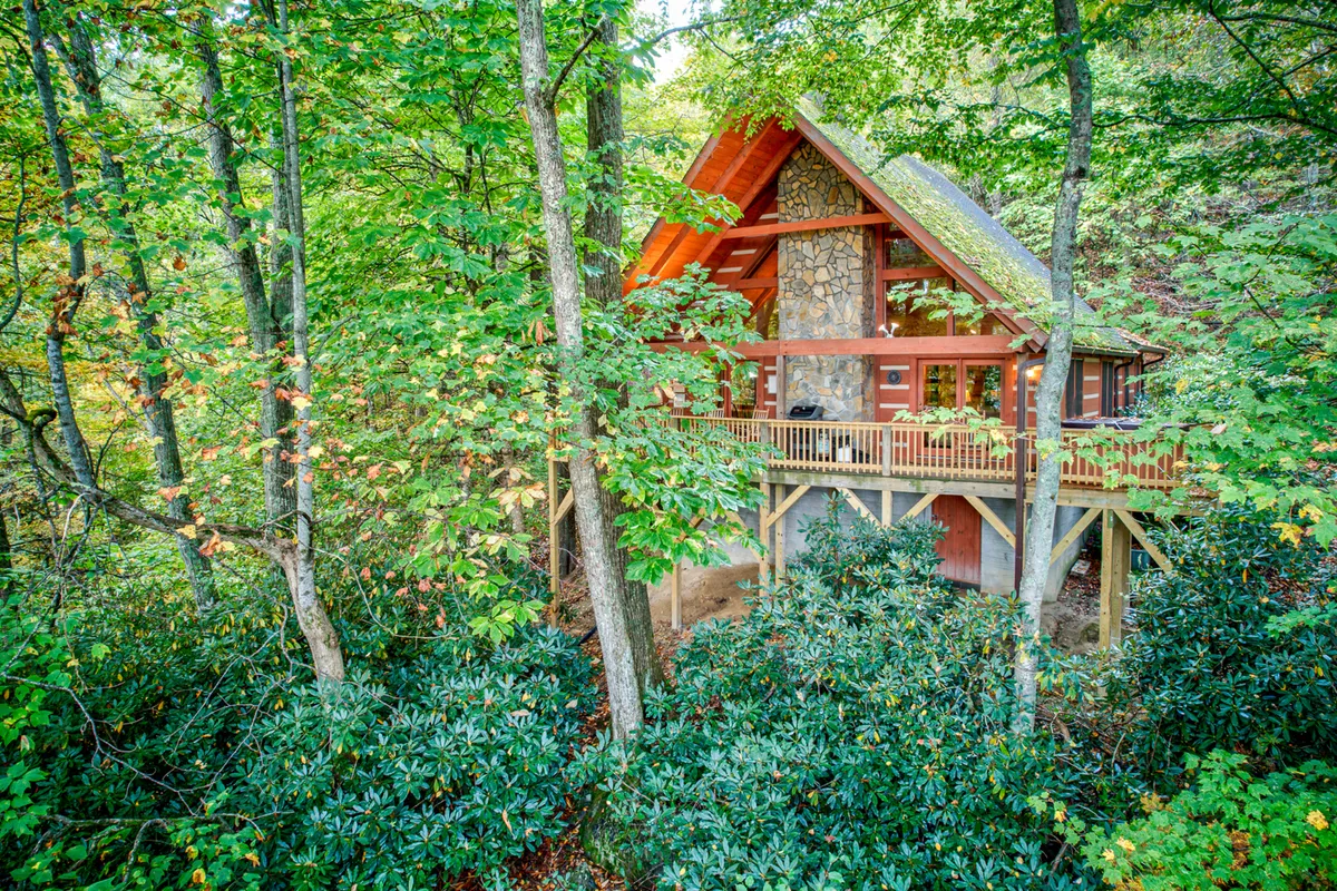 A spacious wooden deck attached to an A-frame cabin, with views over dense foliage and the surrounding forest. The scene radiates a cozy, communal feel, perfect for gatherings, nature watching, or stargazing at night.