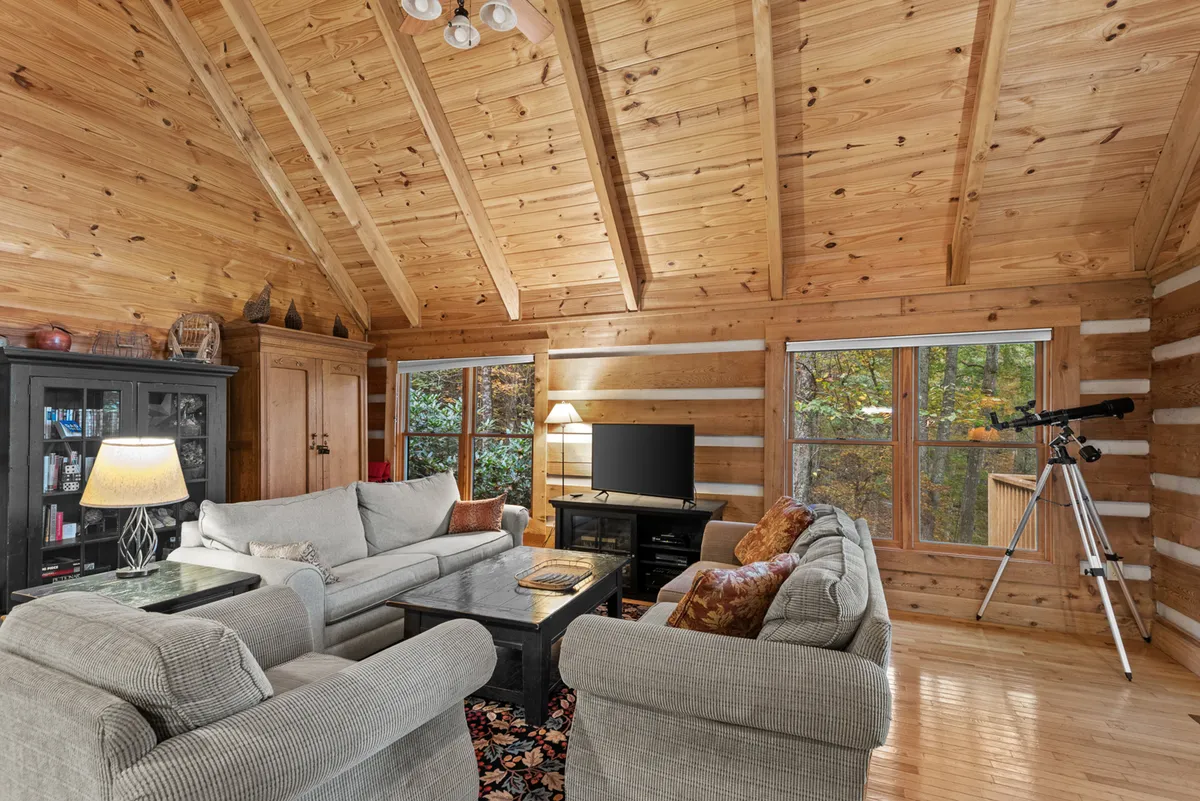 This inviting interior view features a comfortable sofa seating area facing a telescope by large windows, allowing guests to gaze at the stars or wildlife from the comfort of indoors. The wooden ceiling and bookshelves add to the cozy, romantic ambiance.