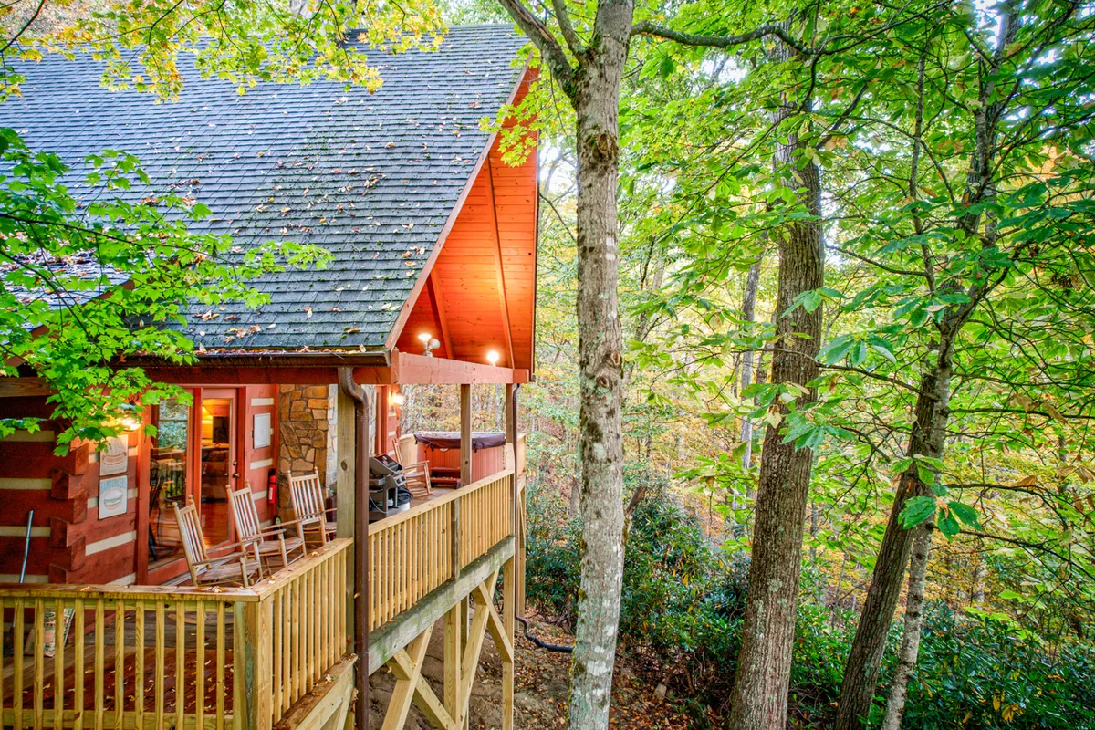 A warm, inviting porch adorned with wooden rocking chairs sits at the forefront of a uniquely designed cabin. Surrounded by lush greenery, the porch offers a perfect spot for sunrise coffee, stargazing, or simply soaking in the peaceful ambiance of the mountains.