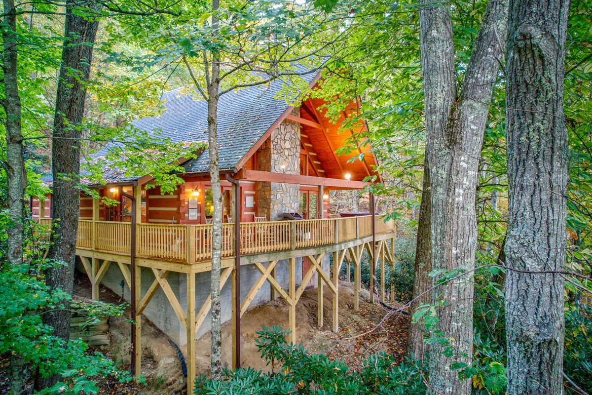 A spacious wooden deck with a stone chimney overlooks a tranquil, tree-filled landscape. The deck is set up for families and friends to gather, dine outdoors, and enjoy the changing seasons. Its vantage point is perfect for sunset views, morning coffee, or nighttime stargazing, encapsulating the year-round adventure the location offers.