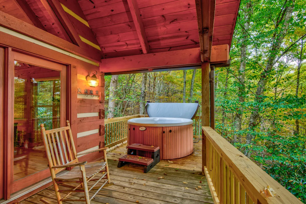 A hot tub and a wooden rocking chair share the spotlight on a deck, surrounded by trees and a wooden railing. The scene is both inviting and intimate, with a strong sense of relaxation and closeness to nature.